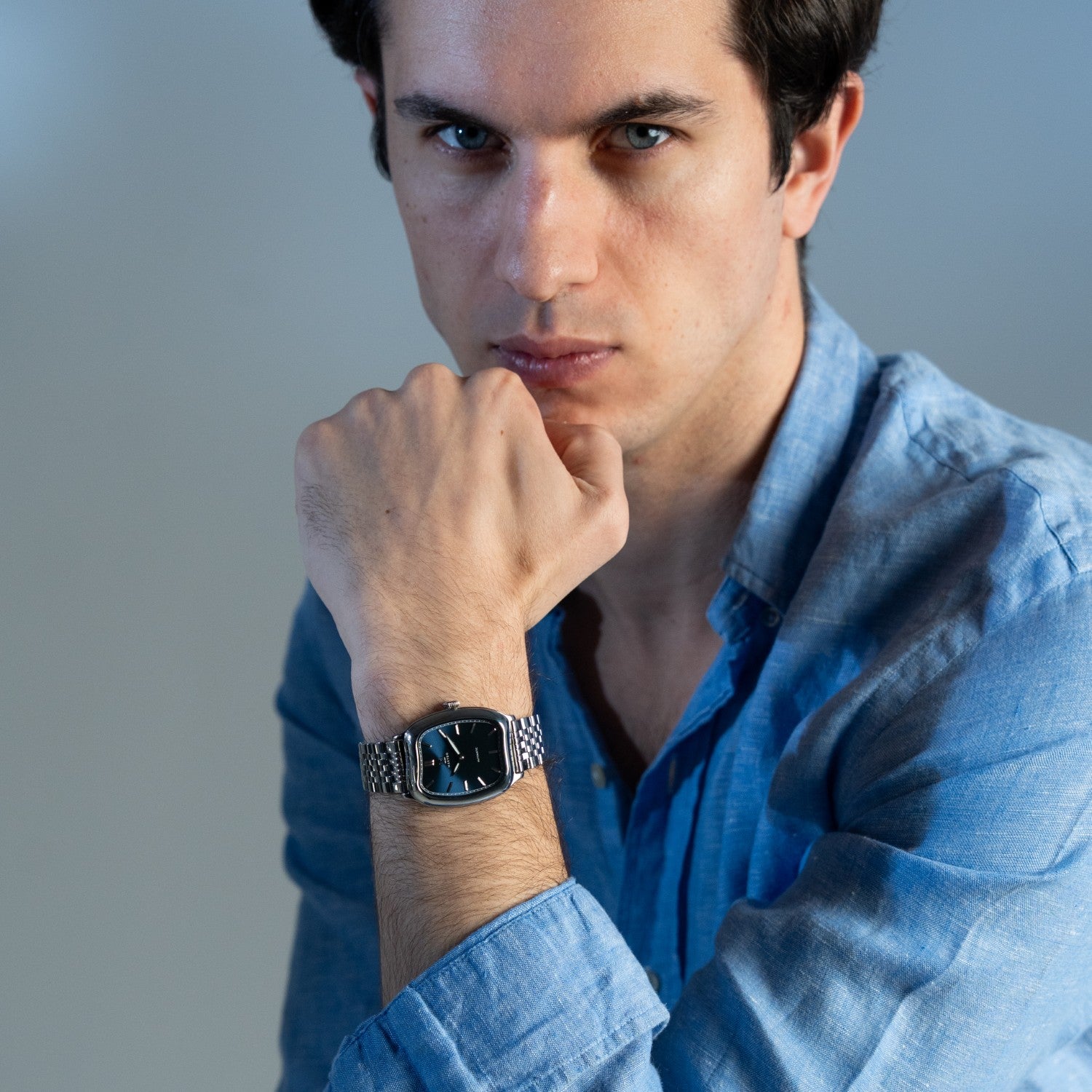 Man wearing a blue shirt and a watch with a gray background