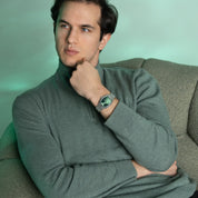Man wearing a green turtleneck sweater sitting on a green couch.