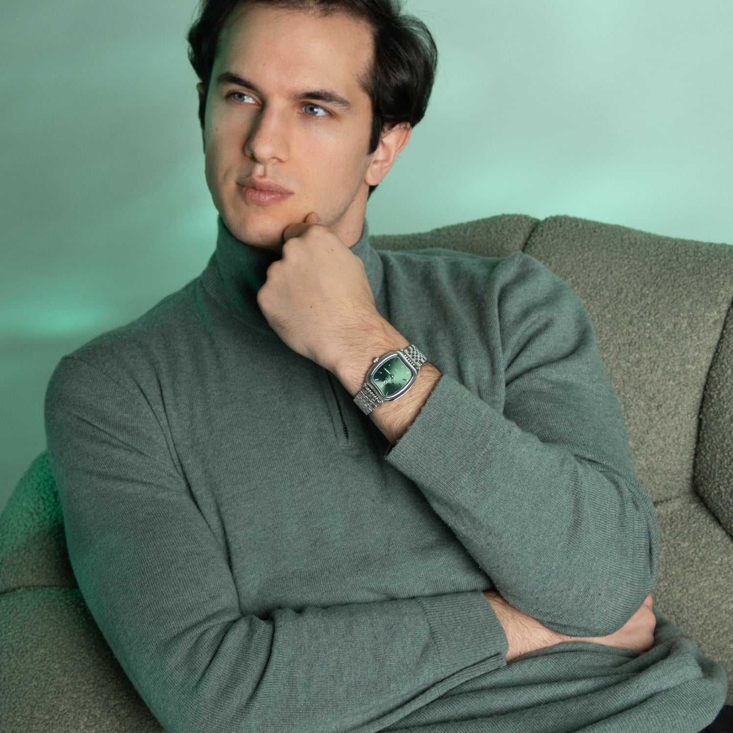 Man wearing a green turtleneck sweater sitting on a green couch.