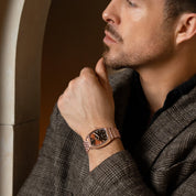 Man wearing a watch with a brown strap and brown face, looking thoughtful.