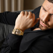 Man wearing a gold watch, sitting on a couch.