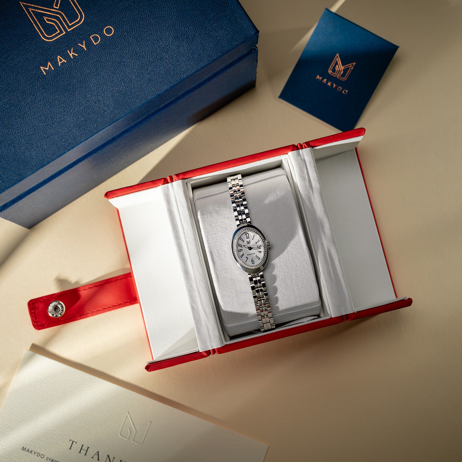 Silver watch in an open red and white box with Makydo branding.